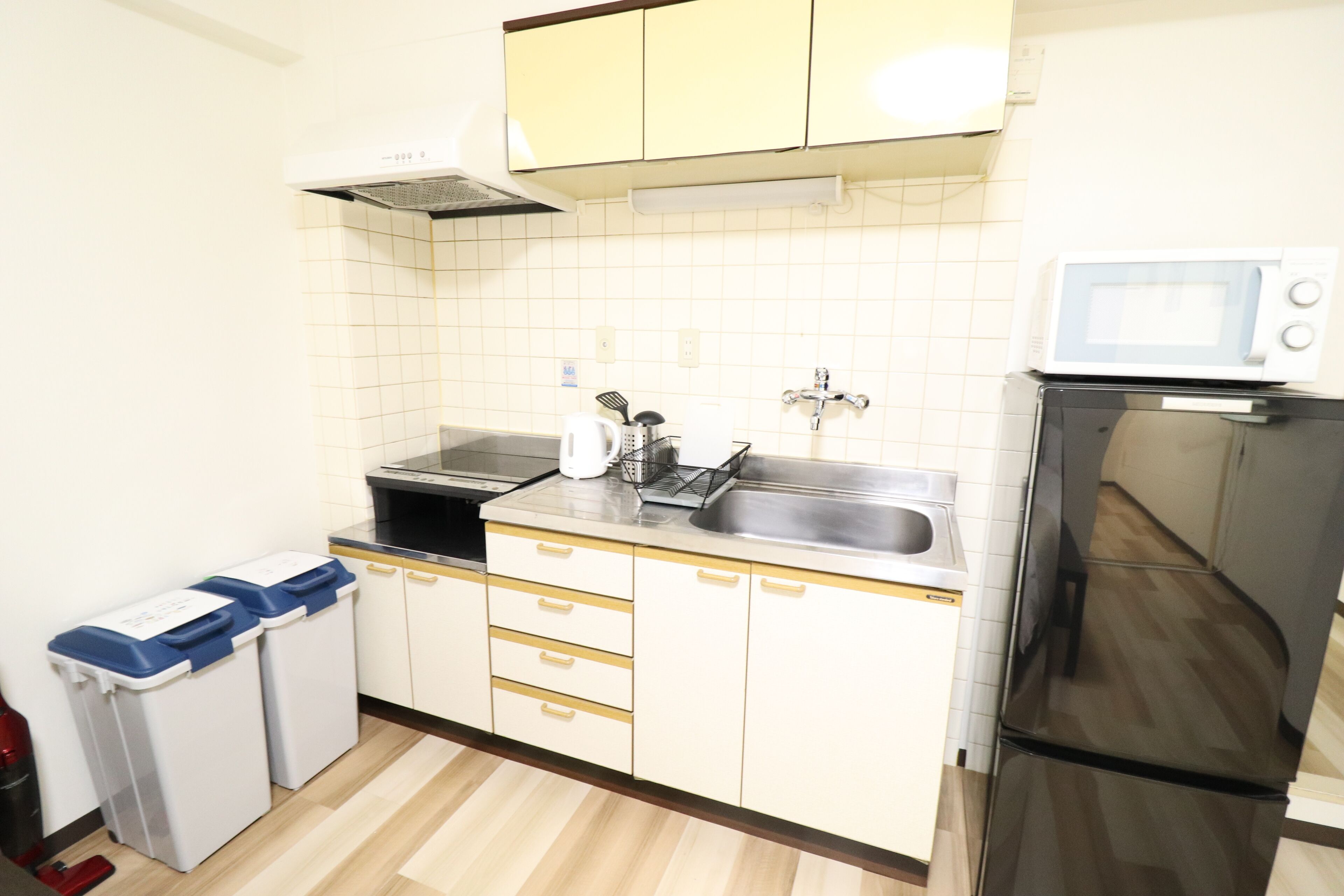 A compact kitchen with white cabinets, a stainless steel sink, a microwave, and a refrigerator.