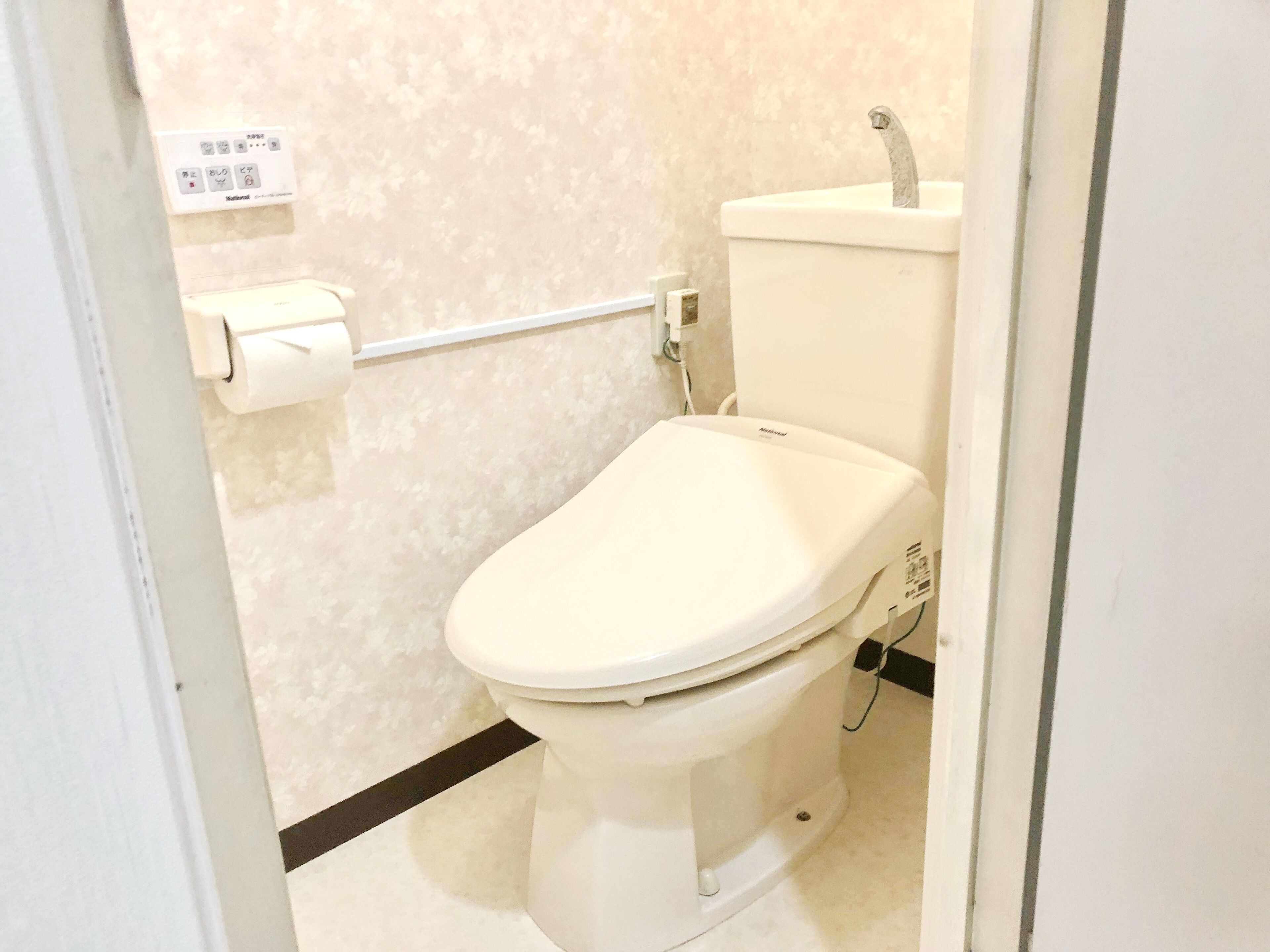 A bathroom with a toilet, a toilet paper holder, and a wall-mounted control panel.
