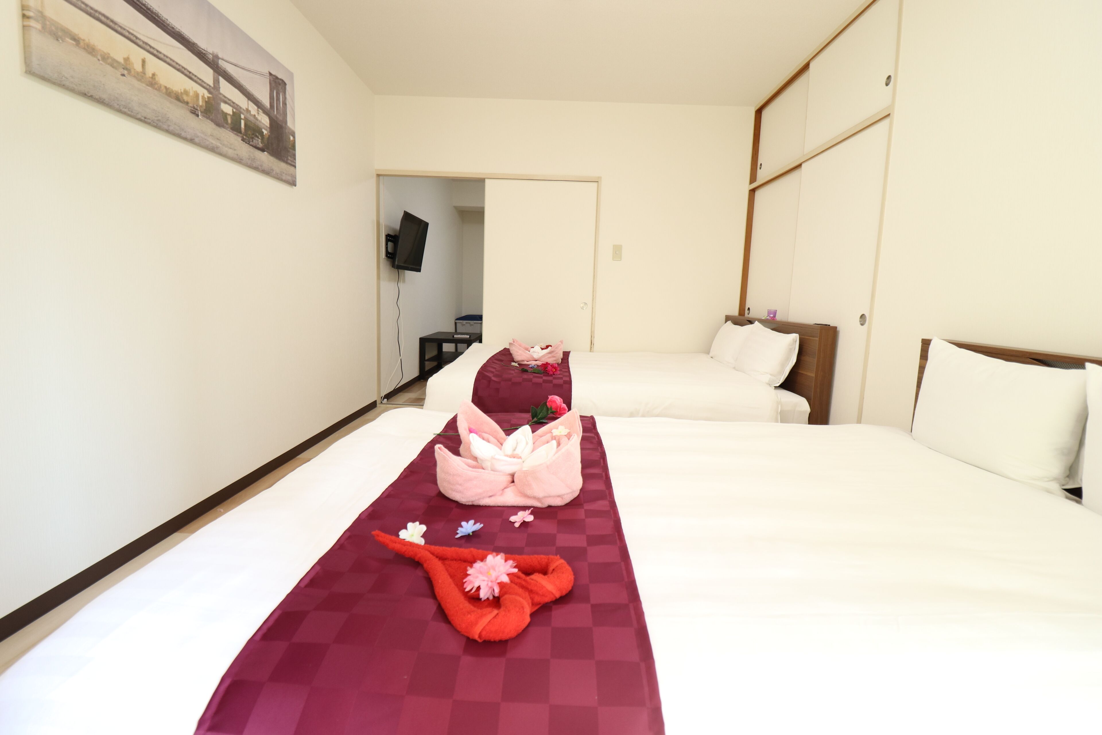 A hotel room with two beds, a checkered red blanket, and a pink towel with flowers.