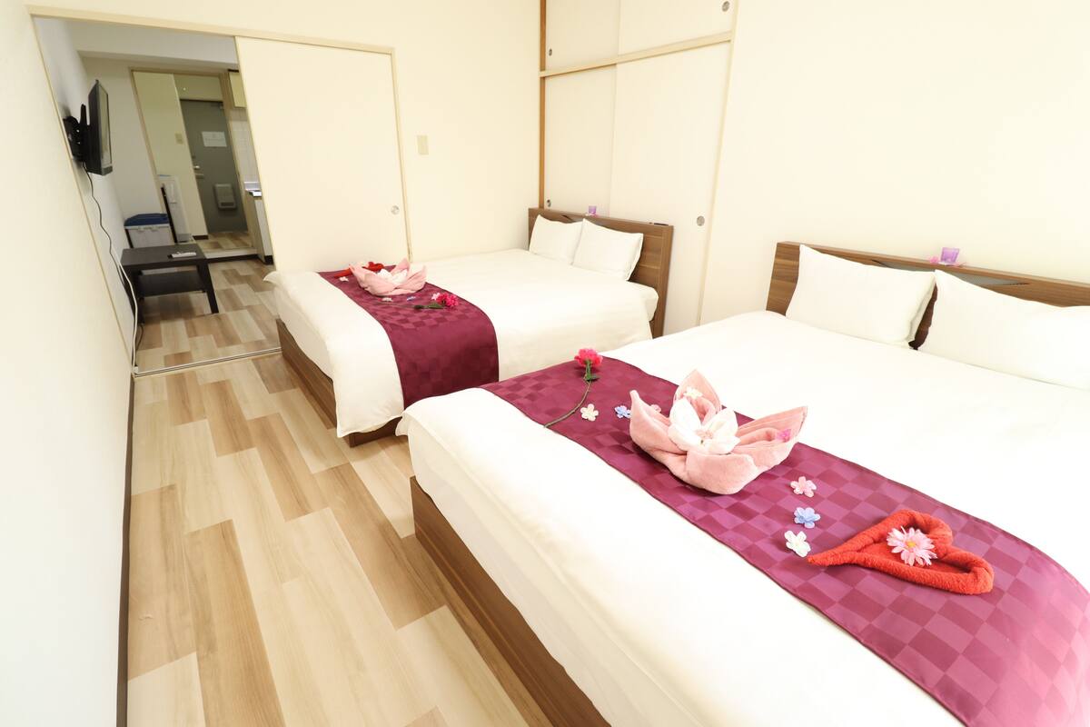A hotel room with two beds, wooden flooring, and a mirror.