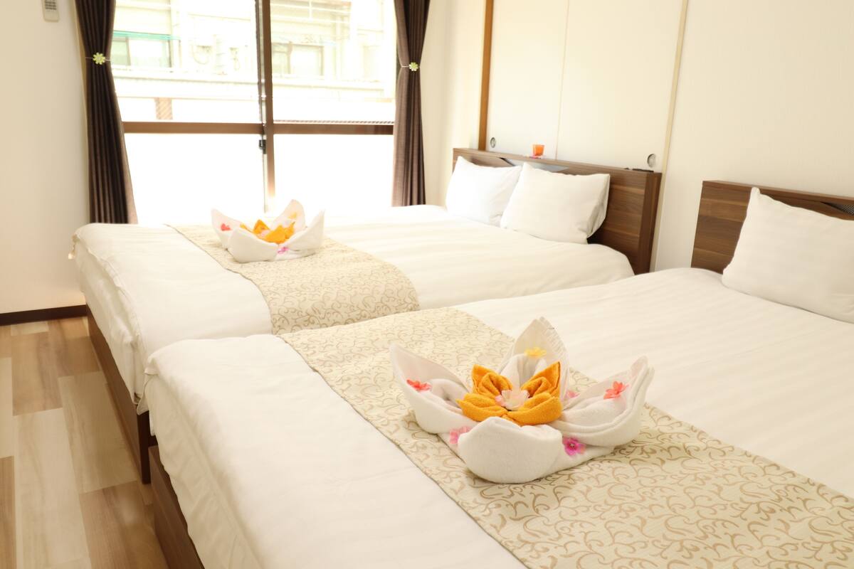 Two neatly made beds with floral arrangements, a wooden headboard, and a window with curtains.