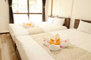 Two neatly made beds with floral arrangements, a wooden headboard, and a window with curtains. - Koto Saiwaicho (Osaka)