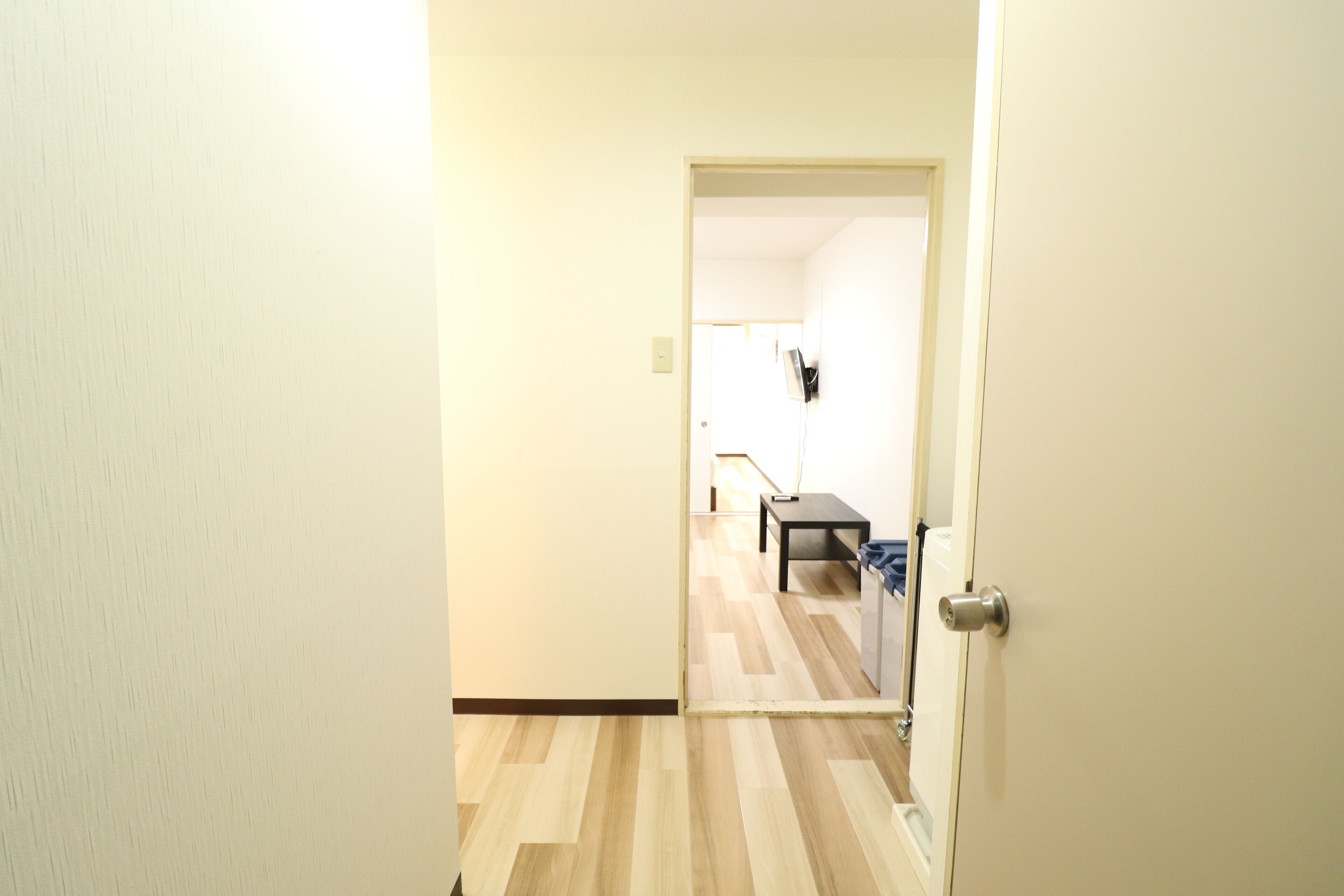 Un pasillo con piso de madera que conduce a una habitación con una cama y una mesita de noche.