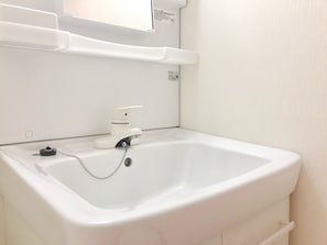A white bathroom sink with a faucet, a soap dispenser, and a small mirror above it. - Koto Saiwaicho (Osaka)