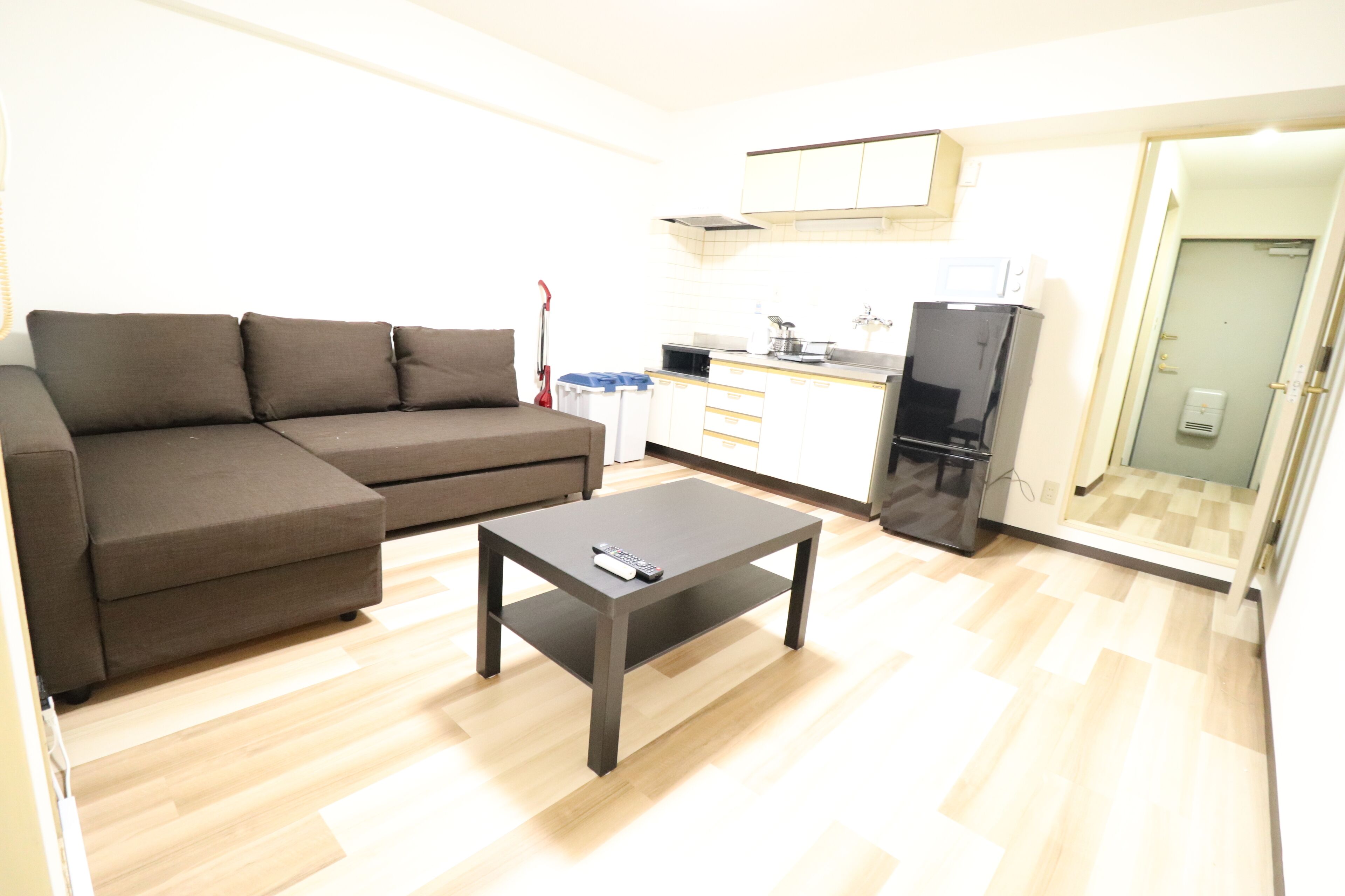 Un espacio habitable compacto con sofá, una mesita de centro, kitchenette y una puerta de vidrio que da a un baño.