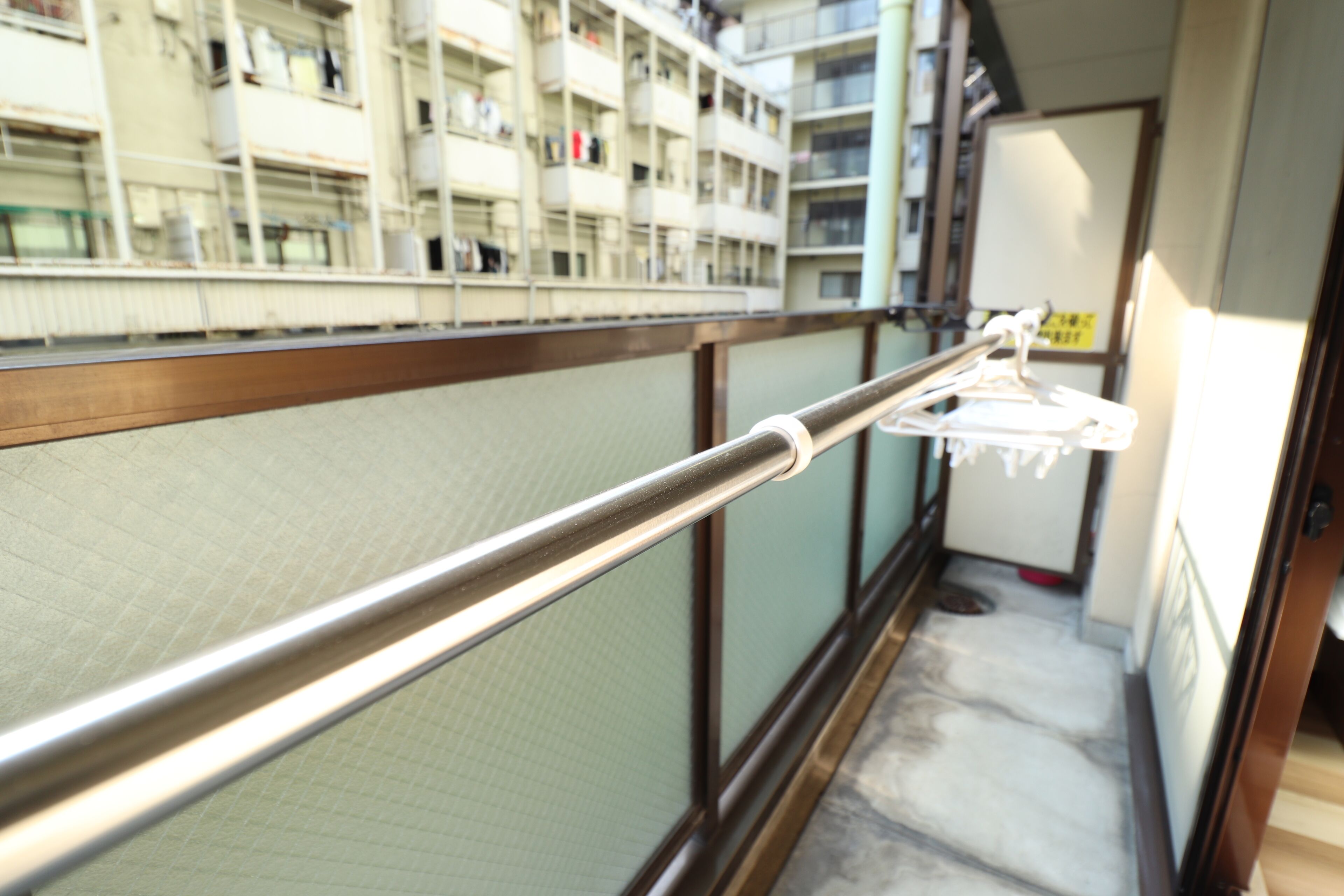 A balcony with a metal railing, a view of a multi-story building with balconies, and a small area with a white object on the floor.