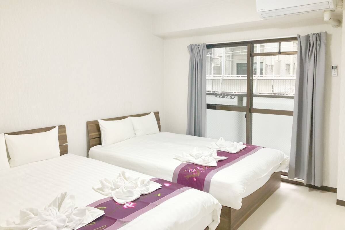 A hotel room with two beds, a window with a view, and an air conditioning unit.