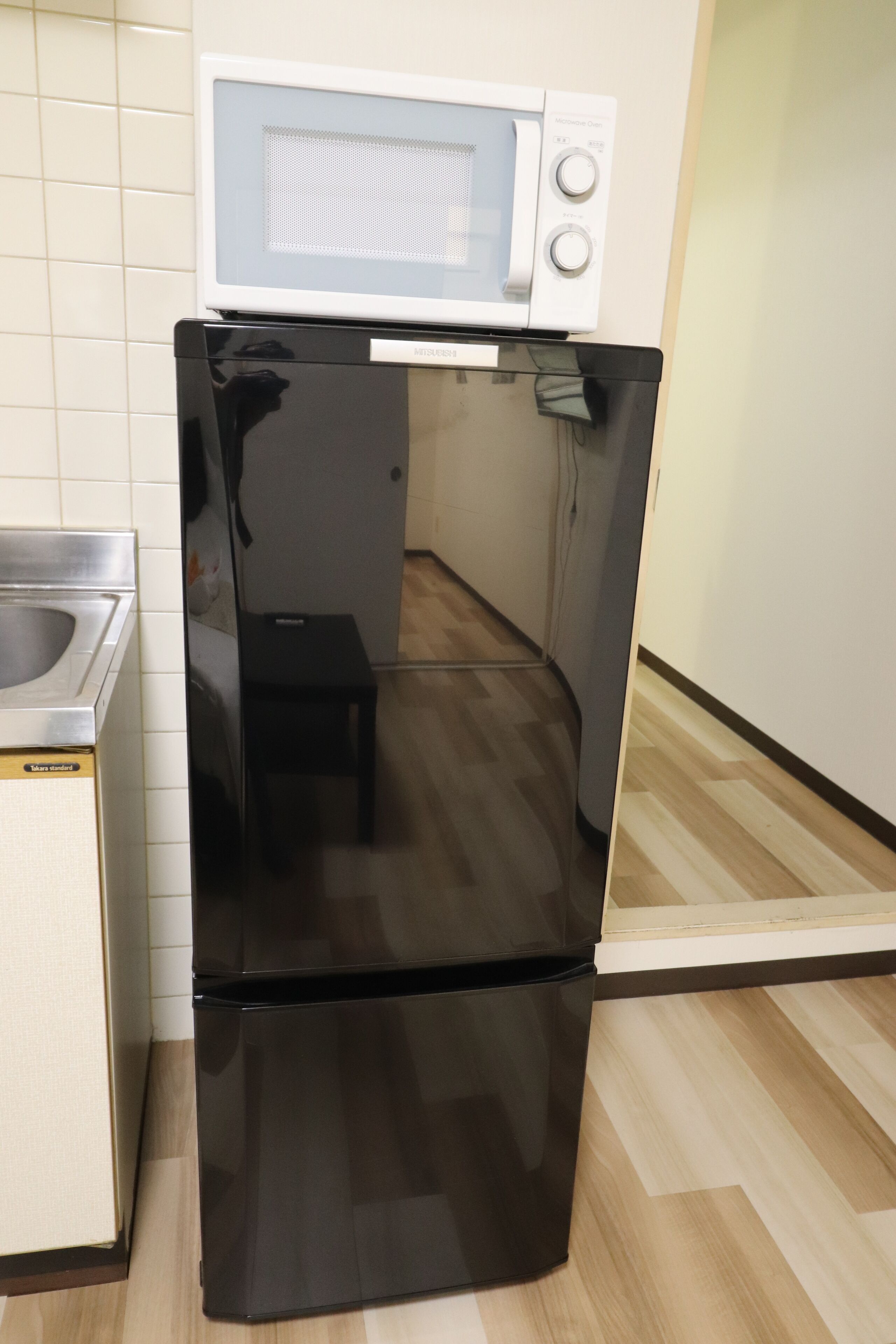 Een compacte keuken met een zwarte koelkast, een magnetron en een klein spoelbakje.