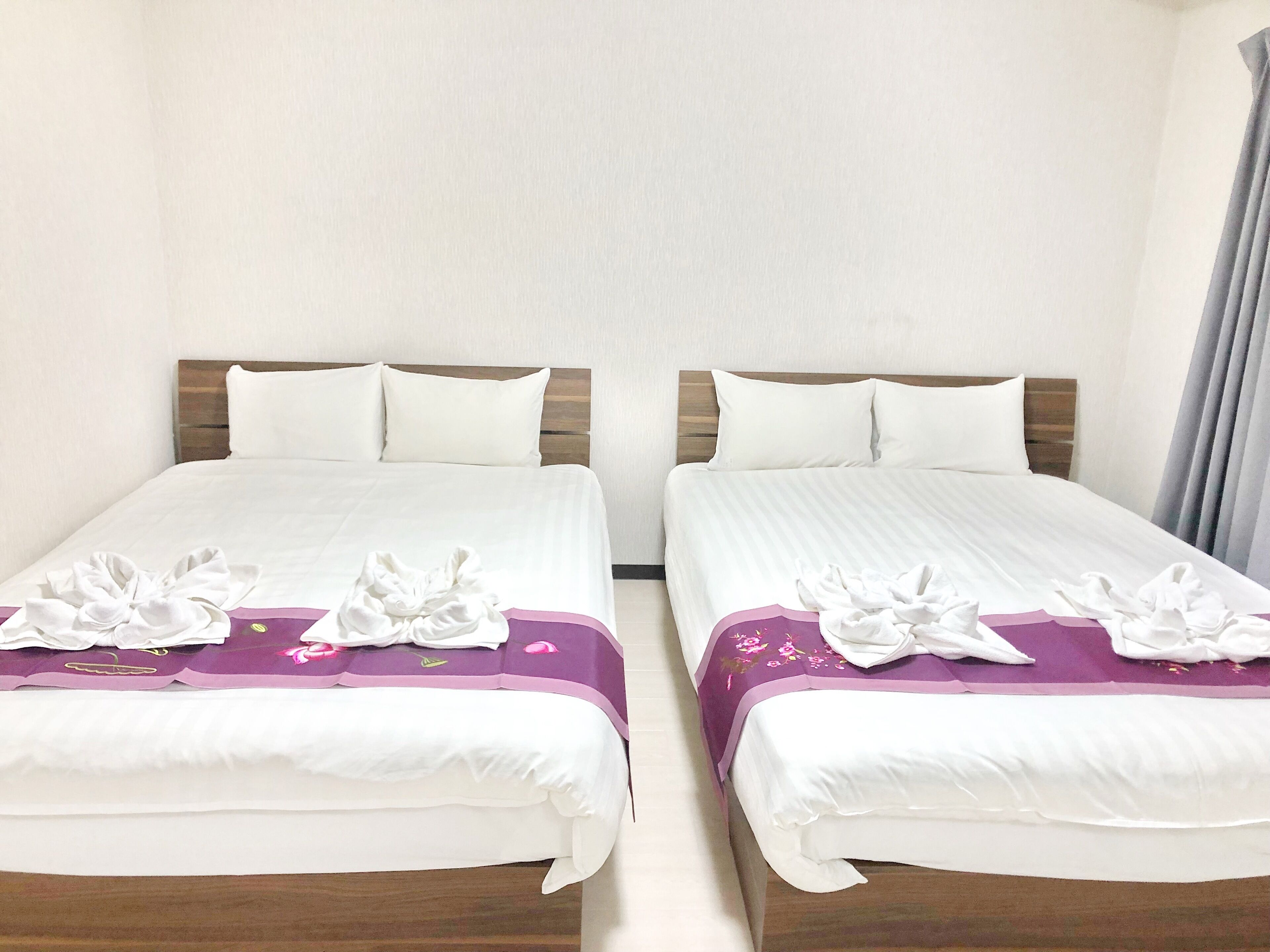 Two twin beds with white linens and purple floral bedspreads, wooden headboards, and white pillows.