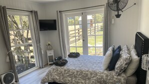 A bedroom with a bed, a TV, a fan, and a view of the outdoors. - Cosy FarmStay@Harmony Cottage on Melbournes' Famous Mornington Peninsula (Tyabb)