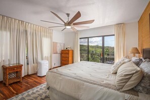 Ein Schlafzimmer mit einem großen Bett, einem Deckenventilator, einer Kommode und einem Fenster mit Blick auf Grünflächen.