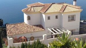 Um edifício branco com telhado ladrilhado, chaminé e vista para o mar.