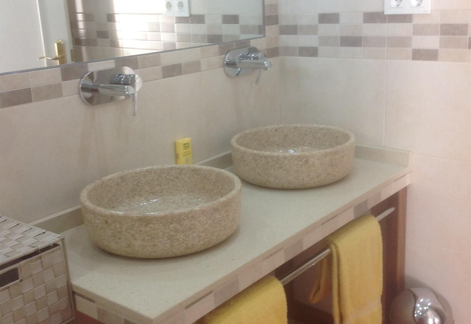 A bathroom with two stone sinks, a mirror, and a yellow towel.