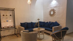 Uma sala de estar com um sofá, duas poltronas, uma mesa pequena, um espelho decorativo e uma prateleira na parede com velas.