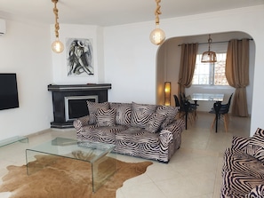 A living room with a zebra-patterned sofa, a glass coffee table, a fireplace, and a dining area with a table and chairs.