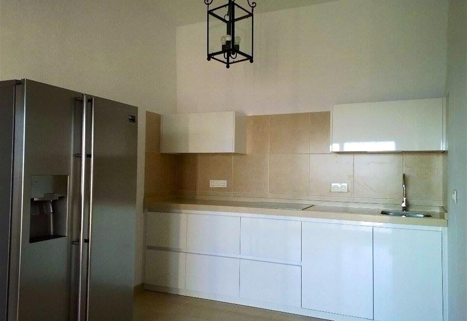 A kitchen with white cabinets, a stainless steel refrigerator, and a pendant light.