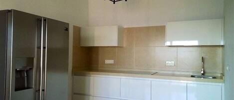 A kitchen with white cabinets, a stainless steel refrigerator, and a pendant light.