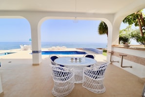 A patio with a pool, white wicker furniture, and a view of the sea.