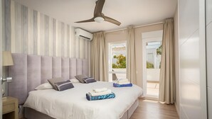 A bedroom with a bed, a ceiling fan, an air conditioning unit, a nightstand, and a view of the outdoors.