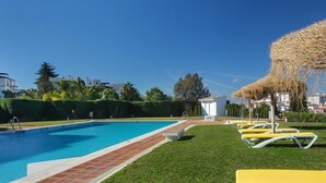 A swimming pool with a clear blue water, surrounded by a well-maintained lawn and yellow lounge chairs.