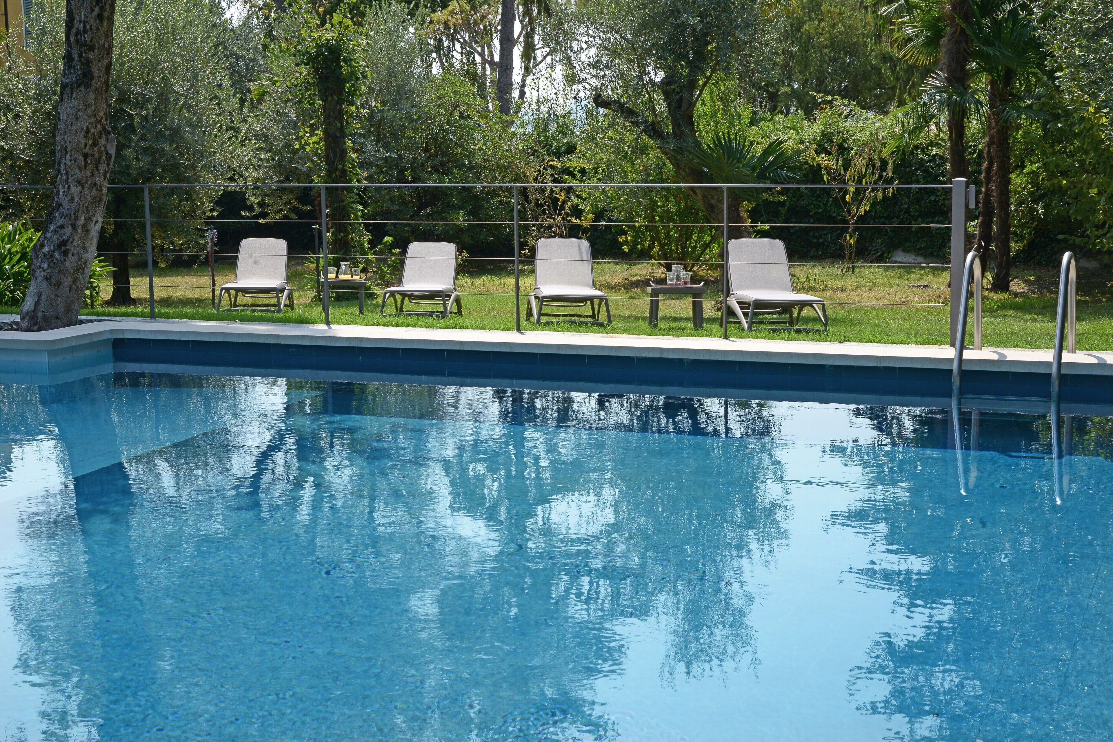 A swimming pool with lounge chairs and a table, surrounded by greenery.