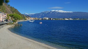 Un paysage côtier avec un bateau amarré près du rivage, un ciel bleu dégagé et une chaîne de montagnes en arrière-plan.