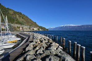 A rocky pier with boats docked, a mountain range in the background, and a clear blue sky. - Lakefront Apartment "Al Segnavento Fasanella" with Pool, Wi-Fi & Garden (Toscolano Maderno)