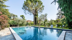 Une piscine rectangulaire bordée de pierres, entourée d’arbres et d’une clôture.