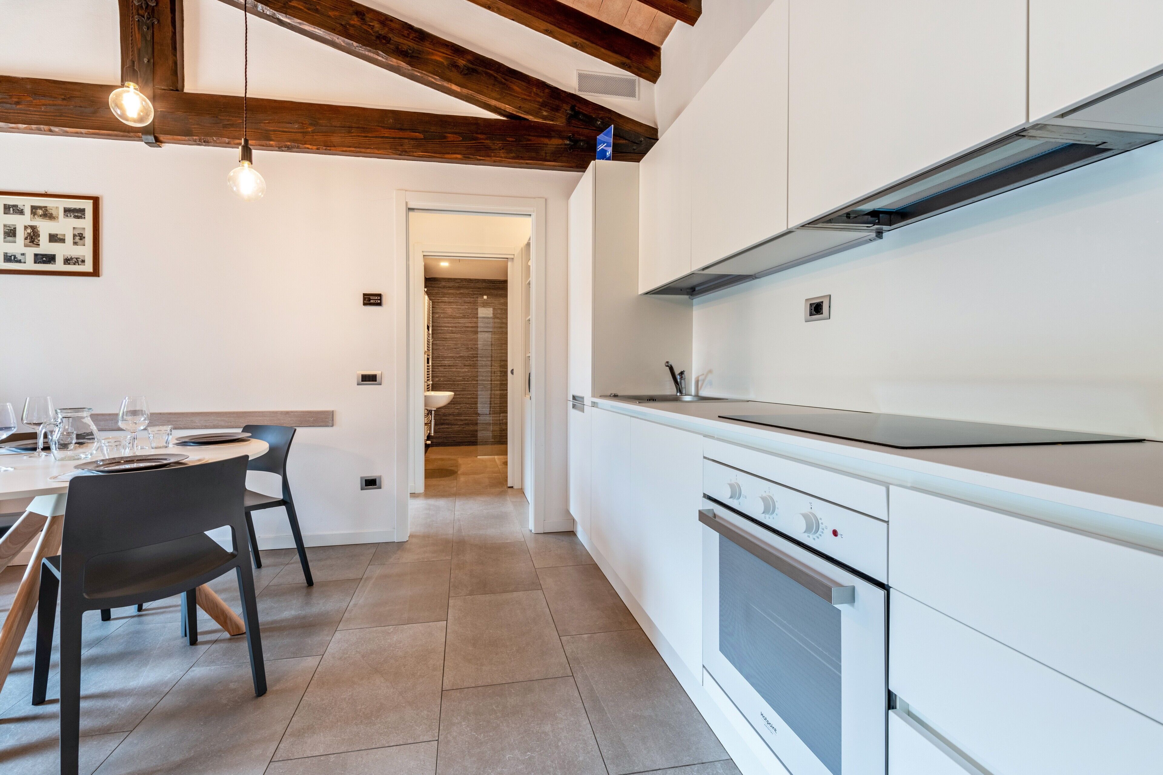 Une cuisine moderne avec des meubles blancs, un four encastré et un coin repas comprenant une table et des chaises.