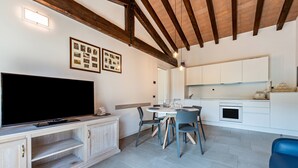 Un salon moderne doté d’un téléviseur à écran plat, d’un meuble de rangement en bois, d’une table à manger avec des chaises et d’un coin cuisine avec des placards et des appareils électroménagers.