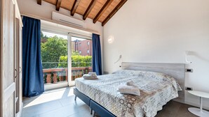 Une chambre avec un grand lit, une porte-fenêtre coulissante donnant sur un balcon et une table de chevet blanche.
