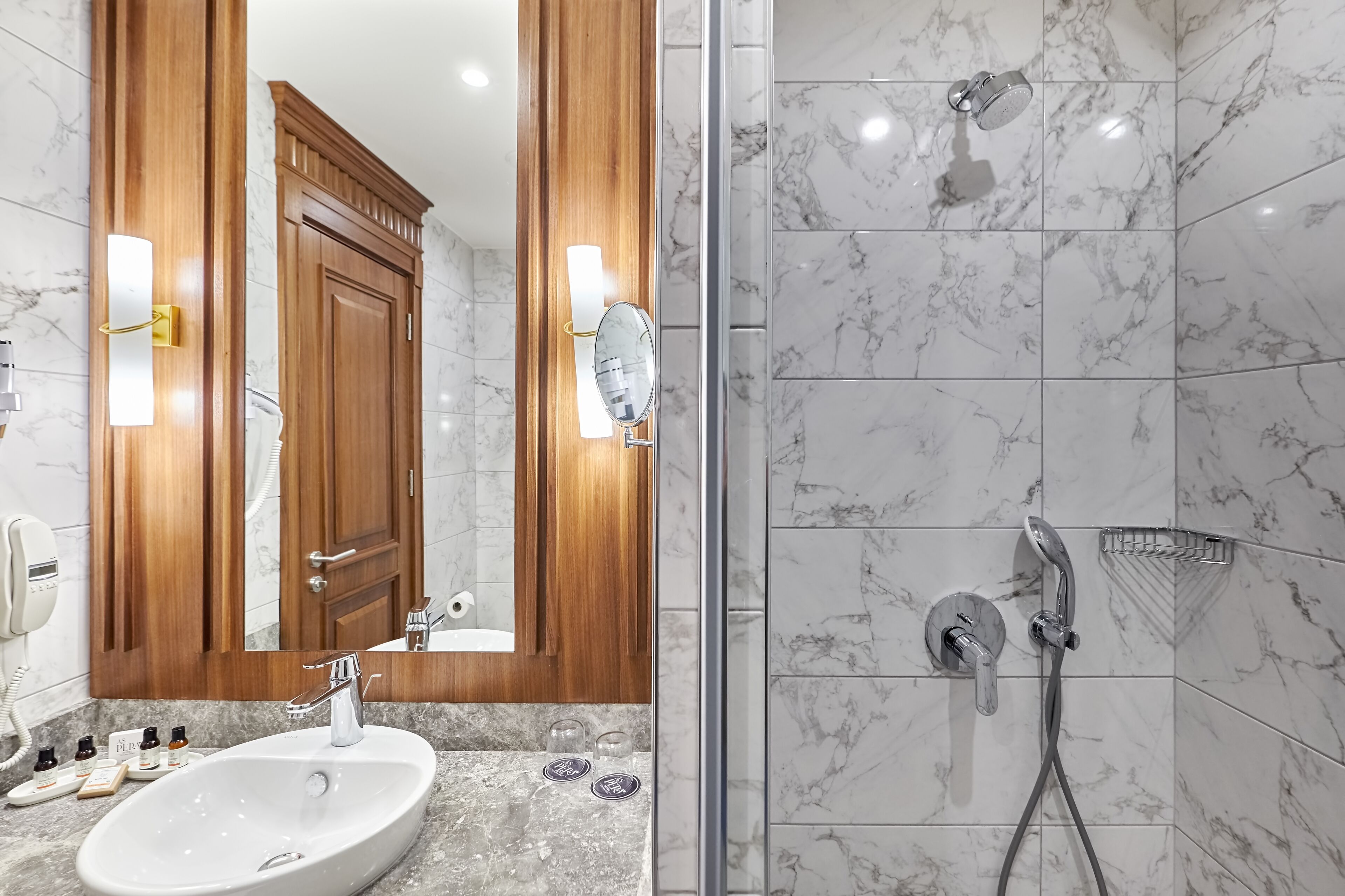Een moderne badkamer met een marmeren wastafel, houten kastjes en een douchecabine met glazen wanden.