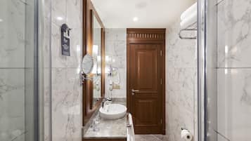 A bathroom with a marble sink, a wooden door, and a glass shower enclosure.
