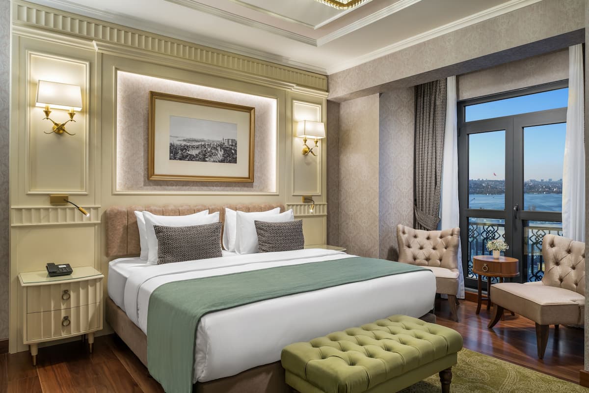 Un dormitorio amplio con una cama grande, dos lámparas de noche, un cuadro en la pared y vistas de la ciudad a través de la ventana.