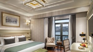 A hotel room with a large bed, a sitting area with a chair and a small table, a view of the city through a large window, and a chandelier. - Aspera Hotel Golden Horn (Istanbul)