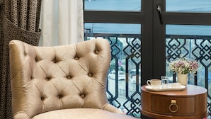 A room with a view of a cityscape through a large window, a tufted armchair, a small wooden side table with a tray, and a vase of flowers. - Aspera Hotel Golden Horn (Istanbul)