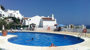 A swimming pool with lounge chairs, a lifebuoy, and a building with white walls and red-tiled roofs. - "Townhouse with Sea View" with Mountain View, Pool, Wi-Fi, Garden & Terrace (Nerja)