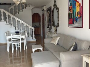 A living room with a staircase, a dining area, and a kitchen in the background.