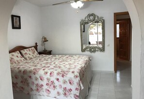 A bedroom with a bed, a nightstand, a lamp, a mirror, and a door leading to another room.