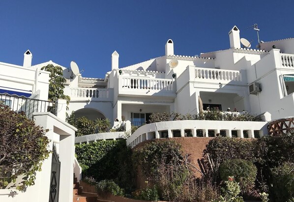 A white building with balconies, a staircase, and surrounding greenery.