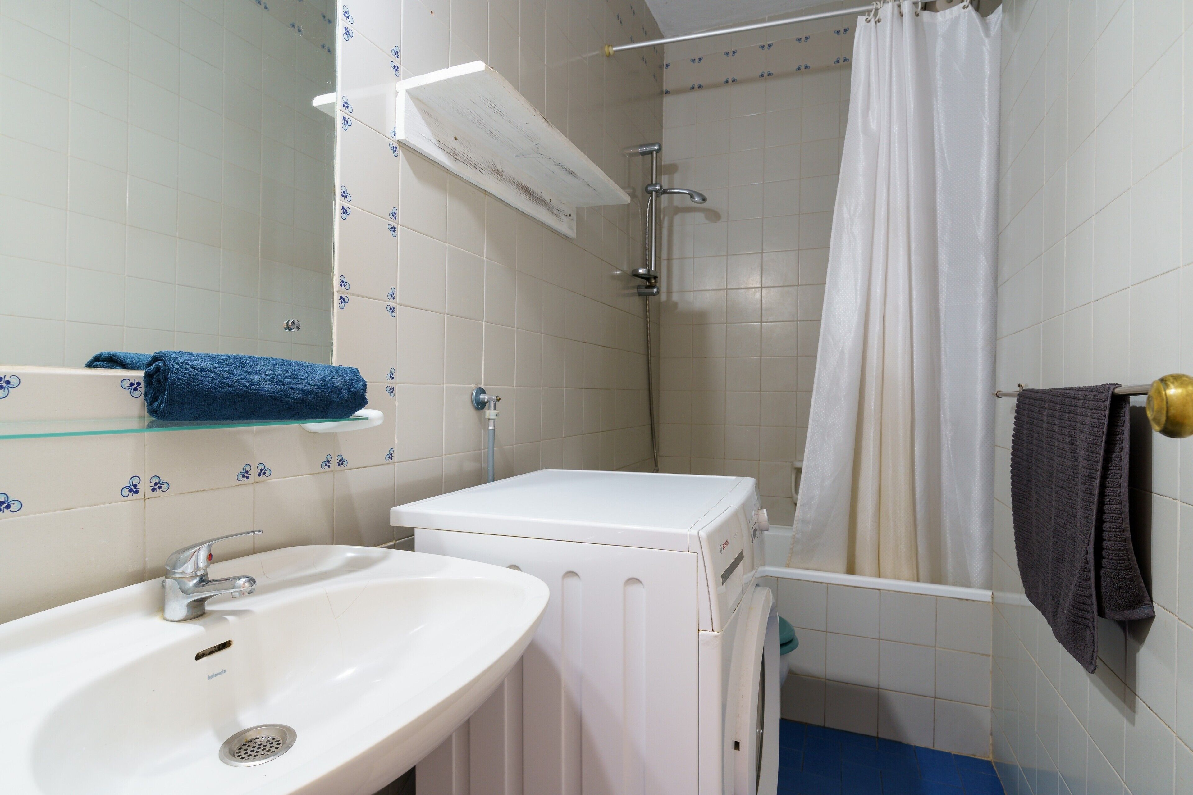 Een badkamer met een wastafel, een wasmachine en een douchehoek.