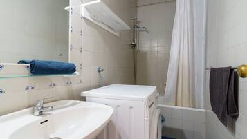 Een badkamer met een wastafel, een wasmachine en een douchehoek.