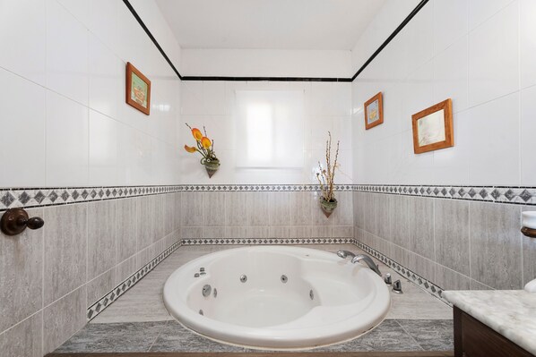 Une salle de bain avec une grande baignoire, des murs carrelés et des tableaux encadrés.