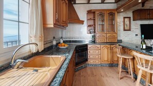 A kitchen with wooden cabinets, a built-in oven, a sink, and a window with a view. - Casa Tijoco – Large Terrace with Views of La Gomera, Air Conditioning, BBQ (Adeje)