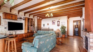 A living room with a sectional sofa, wooden beams, a flat-screen TV, and a fireplace. - Casa Tijoco – Large Terrace with Views of La Gomera, Air Conditioning, BBQ (Adeje)