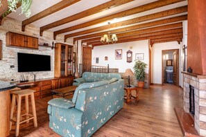 Een woonkamer met een modulaire bank, houten balken, een flatscreen televisie en een open haard.