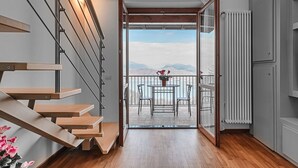 Ein modernes Interieur mit einer Holztreppe, einem Balkon mit Tisch und Stühlen und Blick auf Berge.