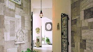 A hallway with stone walls, a decorative relief, a hanging lantern, and a door with a metal gate. - Escape in Central Cattolica (Cattolica)