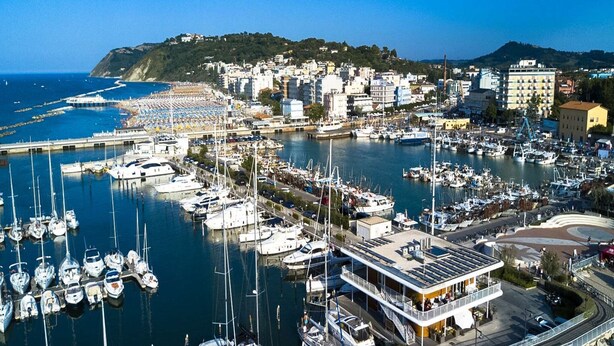 A marina with numerous boats docked, a beach area with umbrellas, and a cityscape in the background. - Escape in Central Cattolica (Cattolica)