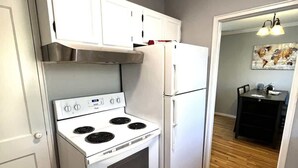Una cocina con electrodomésticos blancos, piso de madera y vista al área de comedor.